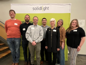 The Solid Light team poses in front of a green Solid Light banner