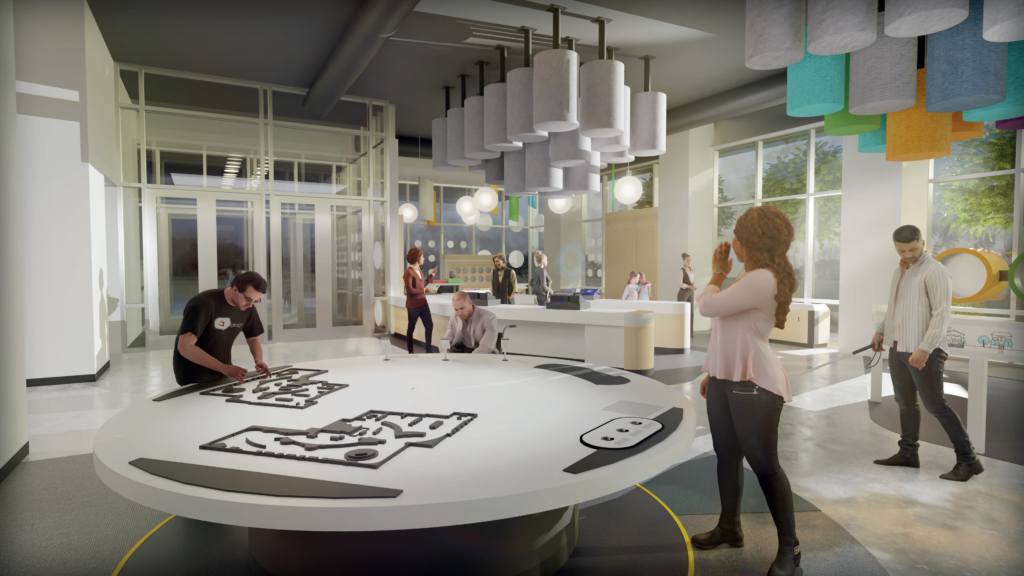The lobby of The Dot Experience. Two people stand at a large, round, white table with tactile floorplans. 