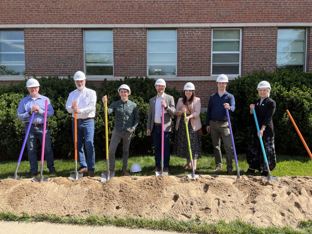 The Solid Light team wearing hard hats and standing on a mound of dirt with colorful shovels ready to break ground on The Dot Experience. 